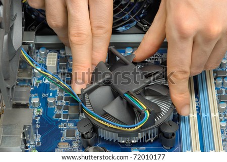 Studio close-up of a technician\'s hands installing a fan on the motherboard