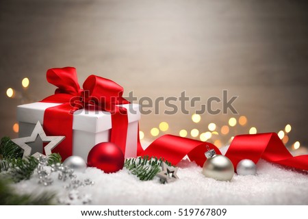 Christmas scene with a white gift box, red bow and ribbon, lights, baubles, fir branches and snow, with copy space
