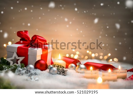 Christmas scene with a white gift box, red bow and ribbon, candles, lights, baubles, fir branches and snow, with copy space