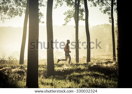 Man running alone in a forest of tree at the sunrise