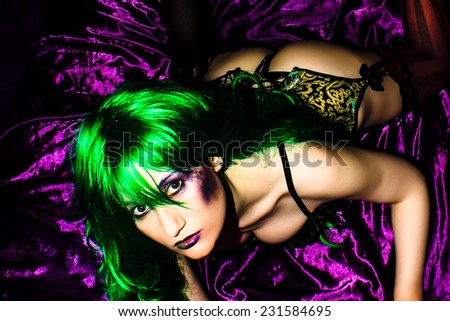 Fetish Female in green basque with green hair and purple & green makeup on purple satin sheets