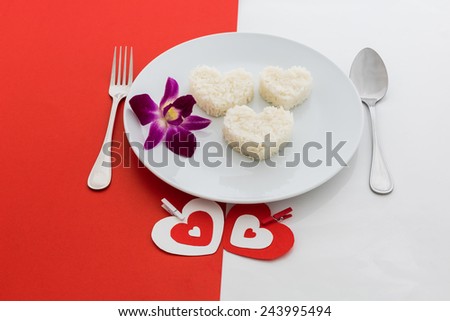 cooked rice heart shapes with a spoon and fork on white dish on half of red and white background