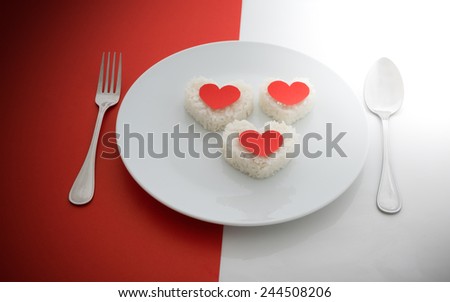 cooked rice heart shapes with a spoon and fork on white dish  half of red and white background