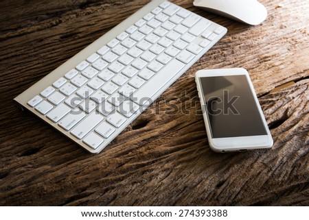 Wireless computer keyboard with the English and Thai alphabet and mouse and smart phone on wooden table