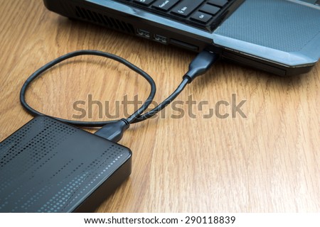 External hard drive connected to laptop on wooden background