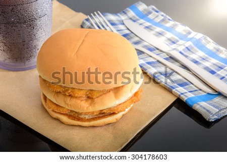 chicken hamburger and glass of cola on brown paper with knife and fork on top table, reflections
