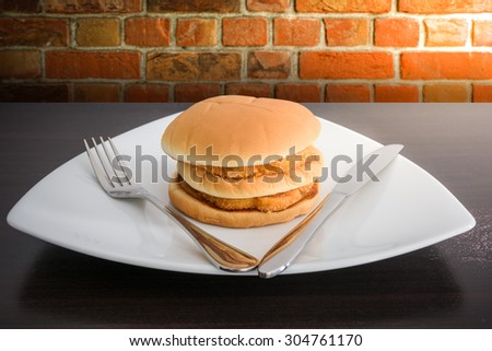 chicken hamburger in white plate  with knife and fork, on top wooden table