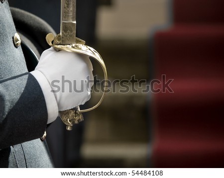 A soldier in military parade uniform holds a cavalry or naval sword