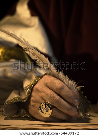 A senior man\'s hand holding a quill and wearing a signet ring with seal