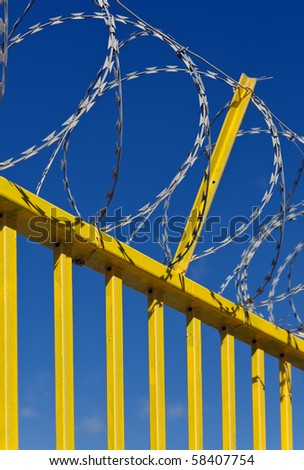 Razor wire on a bright yellow metal barrier against deep blue sky