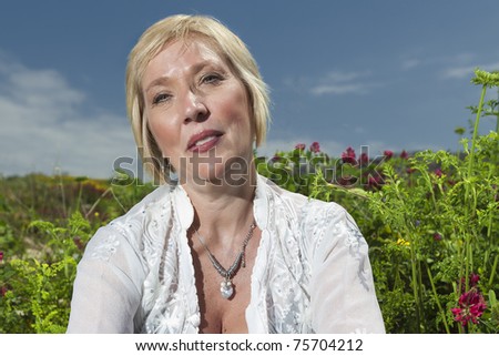 Mature female senior model with blue sky and flowers and foliage in background
