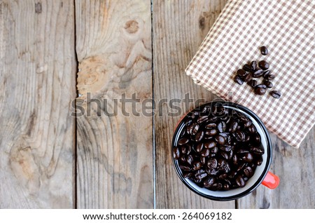 closeup of dark roasted coffee beans in red cup on the wooden table with fabric, focus on coffee beans in red cup