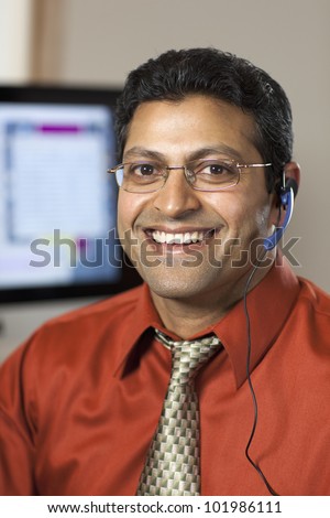 Smiling East Indian customer service representative with headset and computer monitor