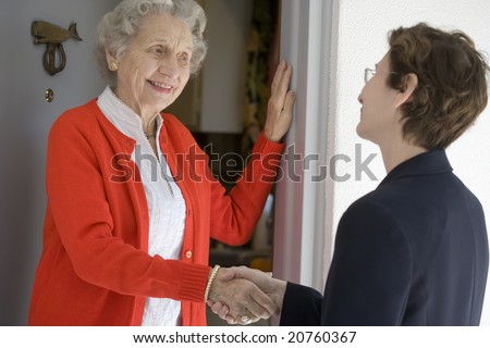 Attractive senior woman shaking hands with visitor at her front door