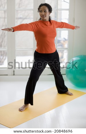Attractive young African American woman in yoga Warrior pose at home