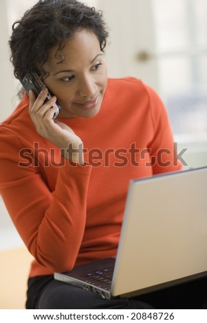 Beautiful young African American woman using cell phone and laptop