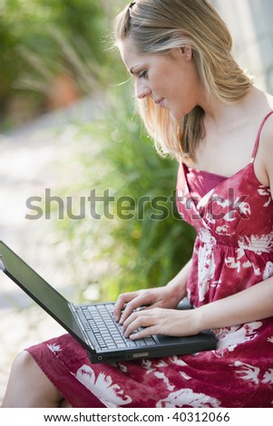 Profile of a young woman using a laptop outdoors. Vertical format.