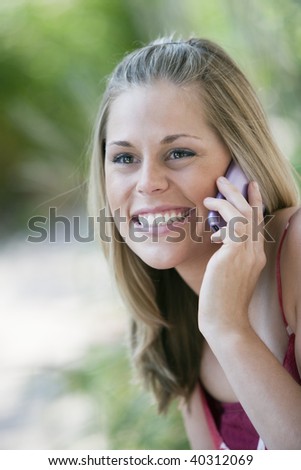 Close-up of a smiling young woman using a cell phone in an outdoor setting. Vertical format.