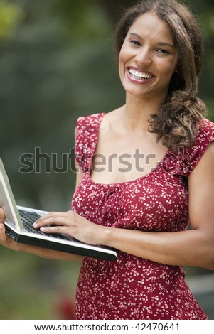 Young woman using laptop in outdoor setting. Vertically framed shot.