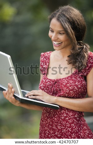Young woman using laptop in outdoor setting. Vertically framed shot.