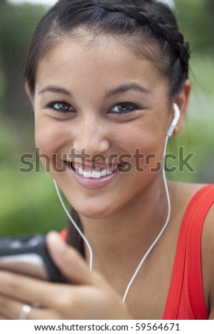 Beautiful Asian woman listens to music on a portable player. She is smiling into the camera outdoors. Vertical shot.