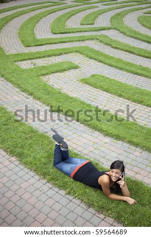 Beautiful young Asian woman lies down on the grass of a park labyrinth while enjoying a conversation on her cellphone. Vertical shot.