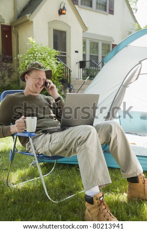 Man camping in his front yard with laptop computer and cell phone