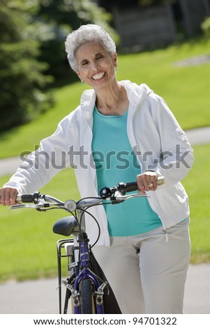 Senior black woman walking her bike through the park