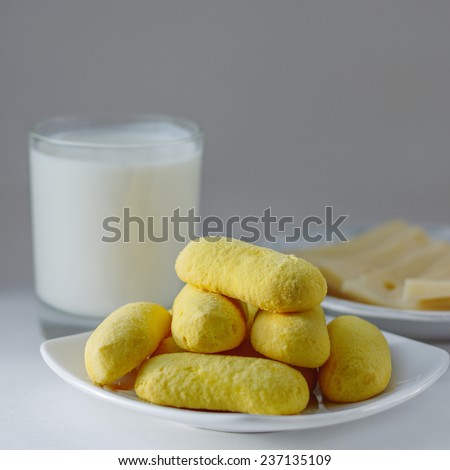 Yellow cookies on a white plate with a glass of milk and cheese