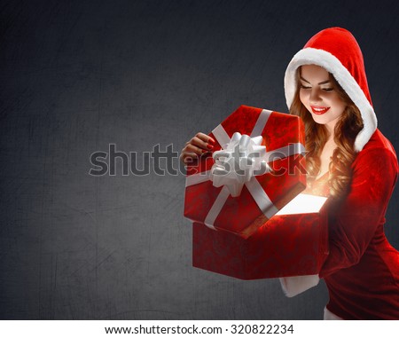 Snow Maiden in red suit smiling holding a gift, opens a gift; on a dark background, portrait.