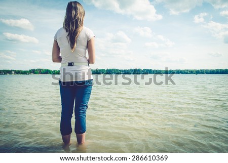 Girl sitting on the pier. Muddy water is visible. Whole scene is somewhat sad and provokes reflection.
