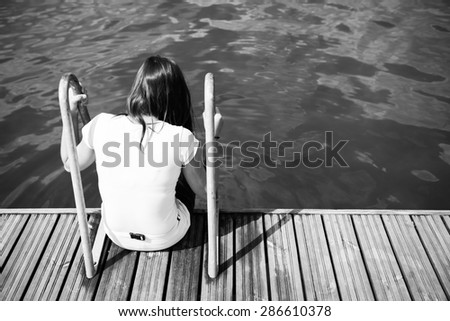 Girl sitting on the pier. Muddy water is visible. Whole scene is somewhat sad and provokes reflection.
