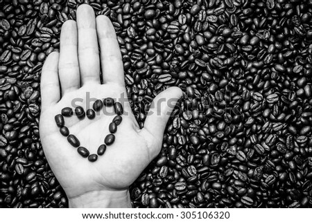 coffee beans heart symbol on top of the hand. Coffee beans texture underneath.