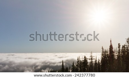 Sunshine in the high alpine over a cloud covered valley and a contrail from a plane under the sun rays