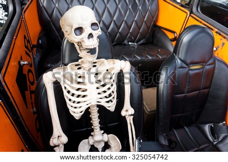 Smiling Skeleton as a passenger ready for a ride in an old car