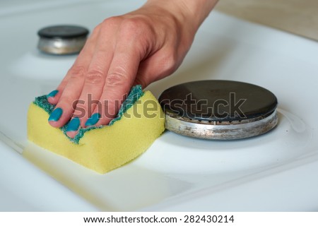 The girl washes a gas stove yellow sponge