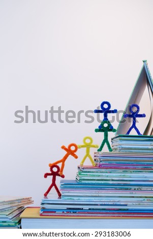 A rainbow of pipe-cleaner people walking up a stack of books as if they are climbing to success through the gaining of knowledge. A wonderful photo for multiple purposes for all nationalities.