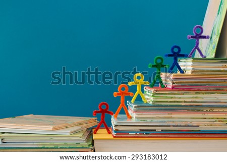 A rainbow of pipe-cleaner people walking up a stack of books as if they are climbing to success through the gaining of knowledge. A wonderful photo for multiple purposes for all nationalities.