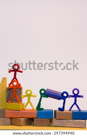 A row of rainbow pipe-cleaner people across children's building blocks with two helping each other to move a block. Wonderful photo for multicultural, international ideas and concepts.