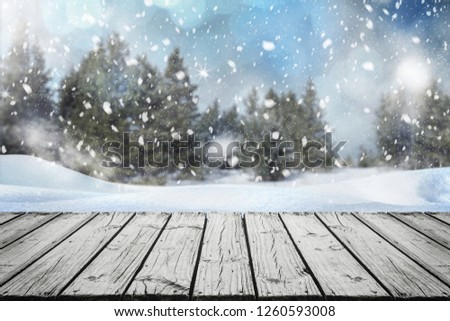 Empty wooden surface for product montage with falling snow and nice view of Christmas trees in winter time.