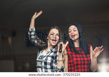 Portrait of happy girls singing in microphone in the karaoke bar