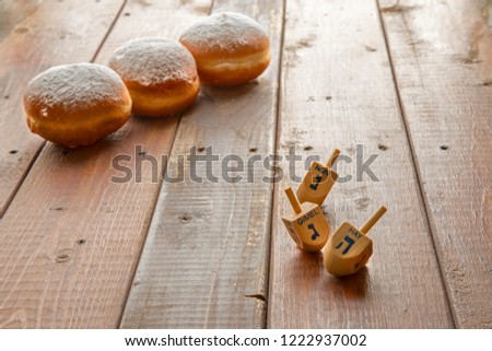 Still life for jewish holiday Hanukkah with 3 donuts and 3 dreidels on wooden rustic table.Hanukkah celebration concept.Shallow DOF Focus on the Deidls