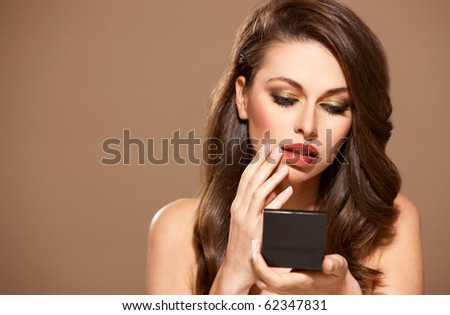 Portrait of a beautiful woman looking into mirror, isolated on beige