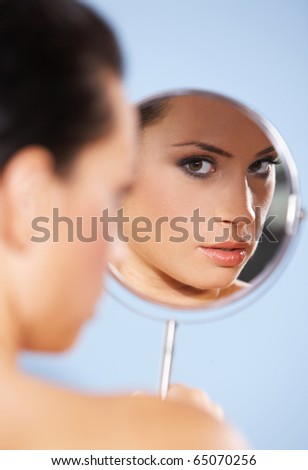 Portrait of beautiful woman, she is looking at the mirror, isolated on blue