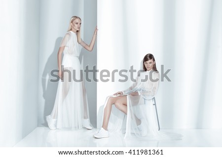 Fashion editorial shot in studio with white background. Two beautiful model posing in total white clothes.