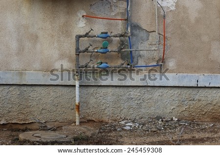 Water meter on a plaster wall of a run-down old common residential house. Unpainted repairs can be seen on the plaster wall.\
 There are signs of rust are on the water pipe.