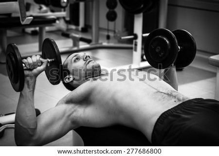 Muscular power athletic male bodybuilder sitting and training his pectoral muscles on bench in fitness center.