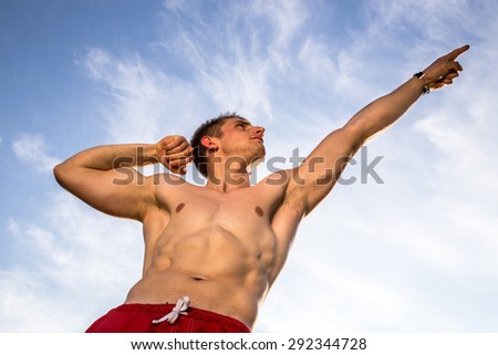 young muscular man pointing at sky