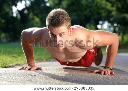 young muscular man push ups on walking road in a park