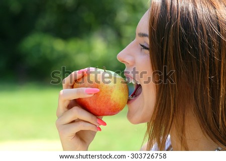 Beautiful young  woman has turned in profile and bites red big apple in a park